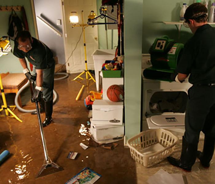 Technicians vacuuming up water from a carpet and moving around items